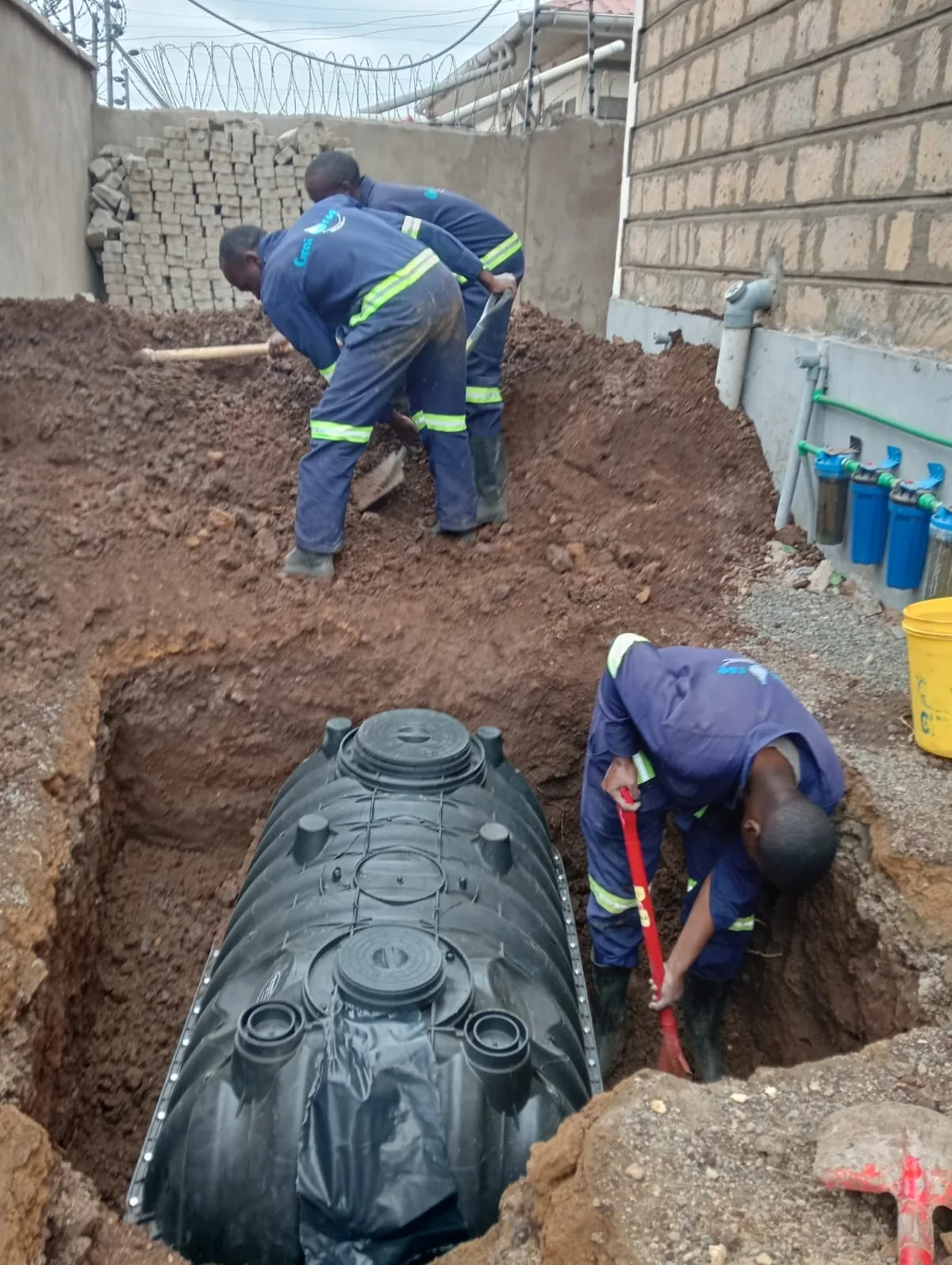 Workers lowering a biodigester tank into an excavated pit
